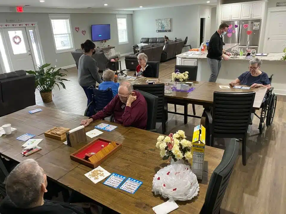 Seniors playing bingo and socializing inside a bright assisted living community common area.