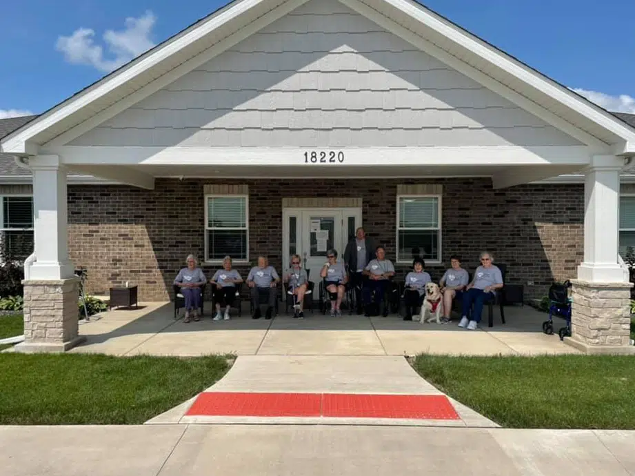 Residents sitting outside the entrance of a senior living community home on a sunny day.