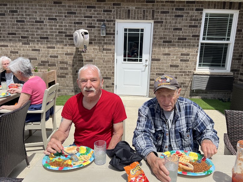 Senior residents enjoying a shared outdoor meal together as part of a social activity at an assisted living home