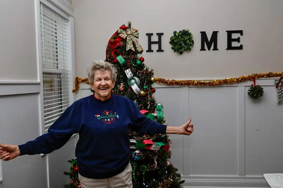 Resident smiling beside holiday decorations and a Christmas tree during a retirement home celebration
