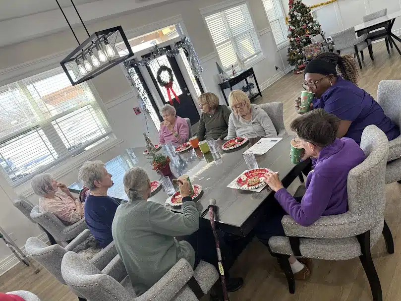 Seniors gathered around a dining table sharing a meal in a small residential assisted living home in Indiana.